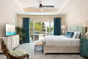 Une chambre à coucher comprenant un lit, un téléviseur, une chaise, un ventilateur de plafond et une vue sur l’extérieur.