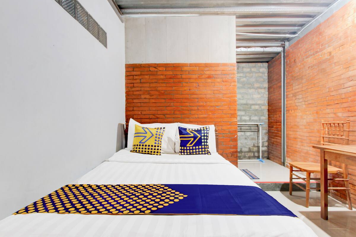 Ein modernes Schlafzimmer mit einem weißen Bett, einer Bettdecke mit blau-gelben Mustern und zwei Kissen mit geometrischen Designs.