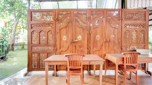 Een houten scheidingswand met gedetailleerde decoraties, een houten tafel en twee stoelen in een overdekte buitenruimte.