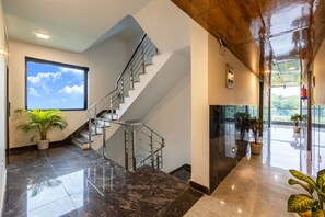 A modern hotel lobby with a marble floor, a staircase with metal railings, and potted plants. - Hotel Admire Inn Sec - 104 By ASPL (Noida)
