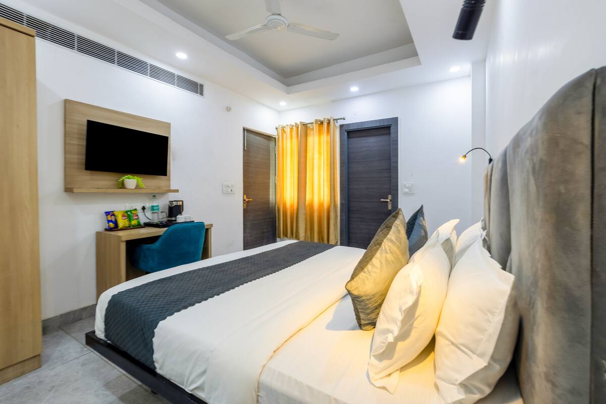 A modern hotel room with a bed, a desk, a television, and a ceiling fan.