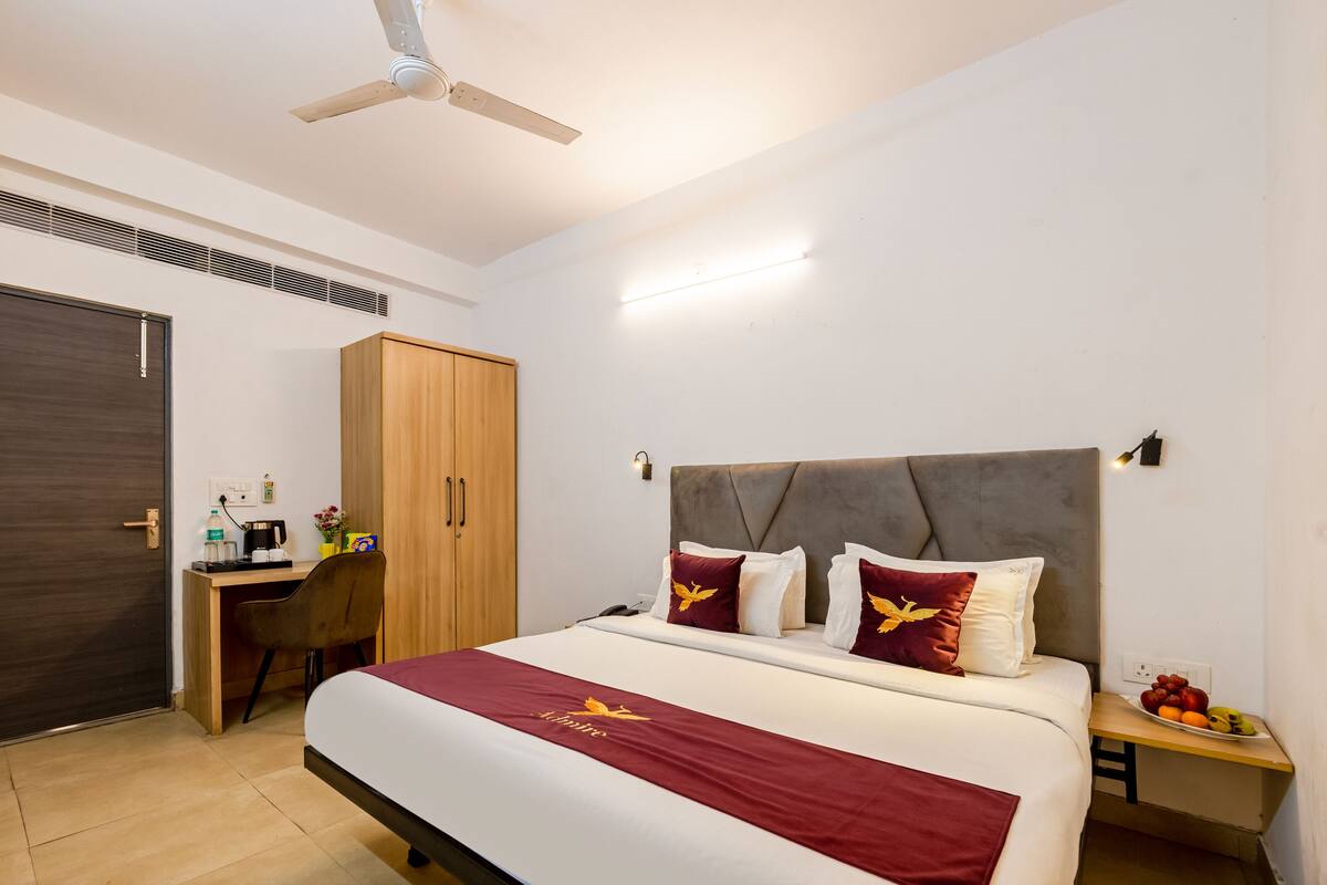 A hotel room with a bed, a desk, a wardrobe, and a nightstand with fruit.