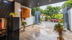 Un espacio exterior moderno con suelo mojado, plantas en macetas, un mueble de madera y un coche rojo al fondo.