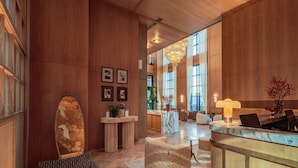 Un vestíbulo amplio con paneles de madera, una recepción, zona de estar y grandes ventanales que dejan entrar luz natural.