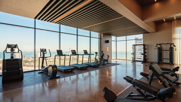 Un gimnasio moderno con amplias ventanas, equipamiento de ejercicio y suelo de madera.