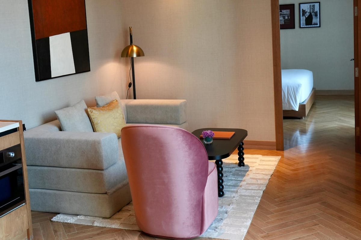 A modern living room with a sofa, a pink chair, a coffee table, and a lamp.