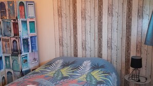 A bedroom with a bed, a wall with vertical wooden planks, a wall-mounted lamp, and a decorative wall piece. - A cosy little nest (Droisy)
