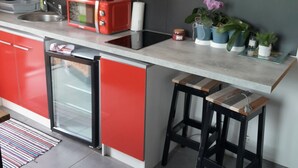 A modern kitchen with red cabinets, a microwave, a small refrigerator, and a coffee maker. There are potted plants on the counter and a world map on the wall. - A cosy little nest (Droisy)