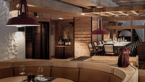 A restaurant with wooden interiors, a long dining table, and hanging red pendant lights. - VAYA Lechtal (Elbigenalp)