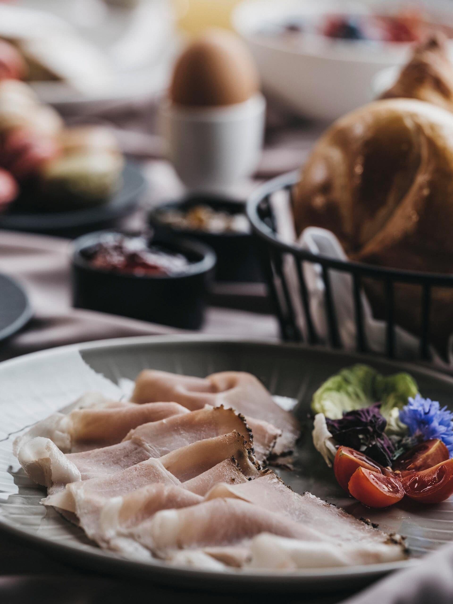 A plate of sliced meat, a bowl of soup, and a basket of bread on a table.