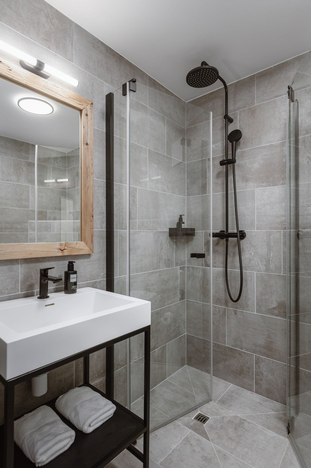 A modern bathroom with a glass-enclosed shower, a white sink, and a wooden vanity.