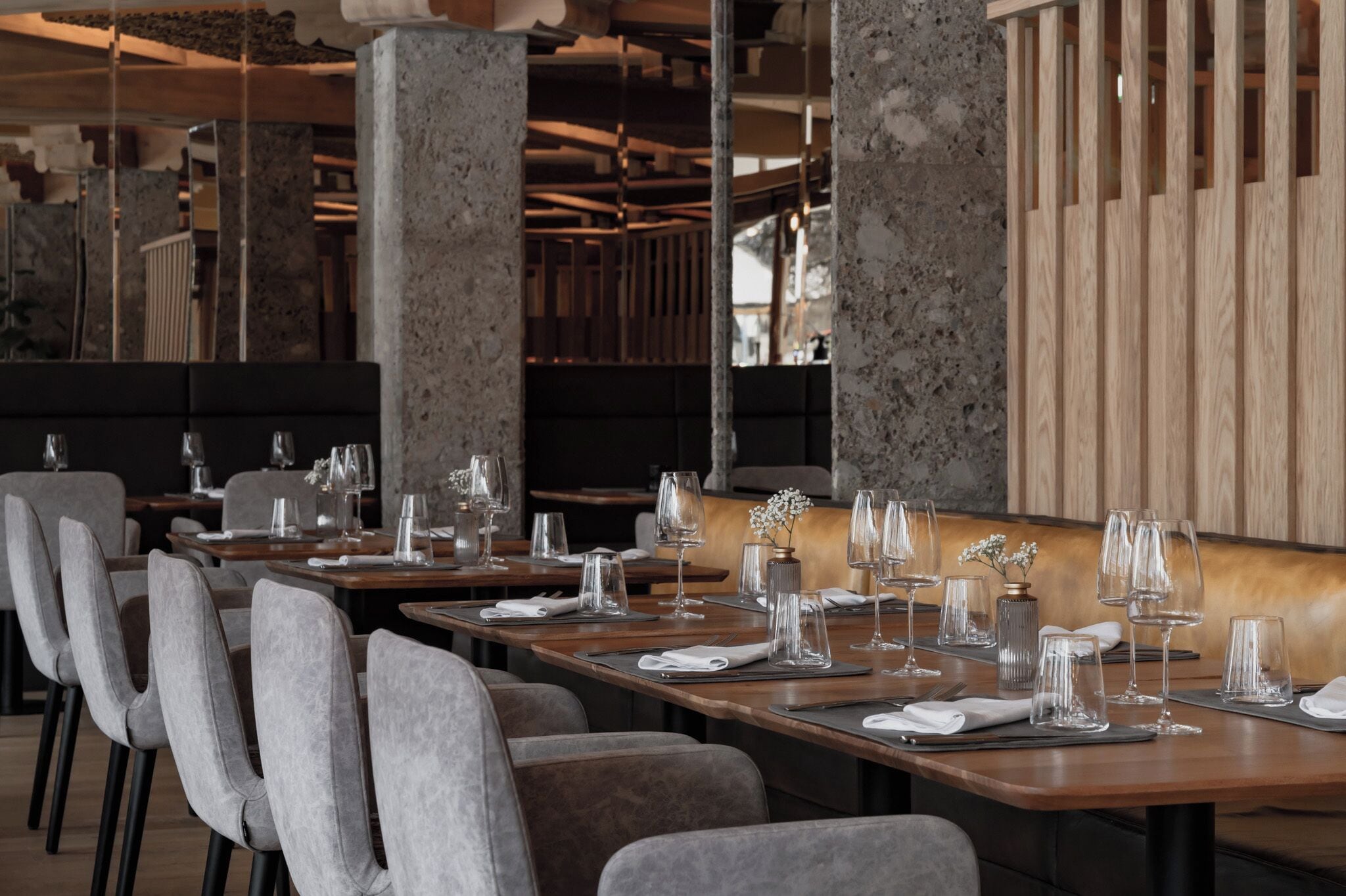 A restaurant with long tables set for dining, featuring grey upholstered chairs and wooden tables.