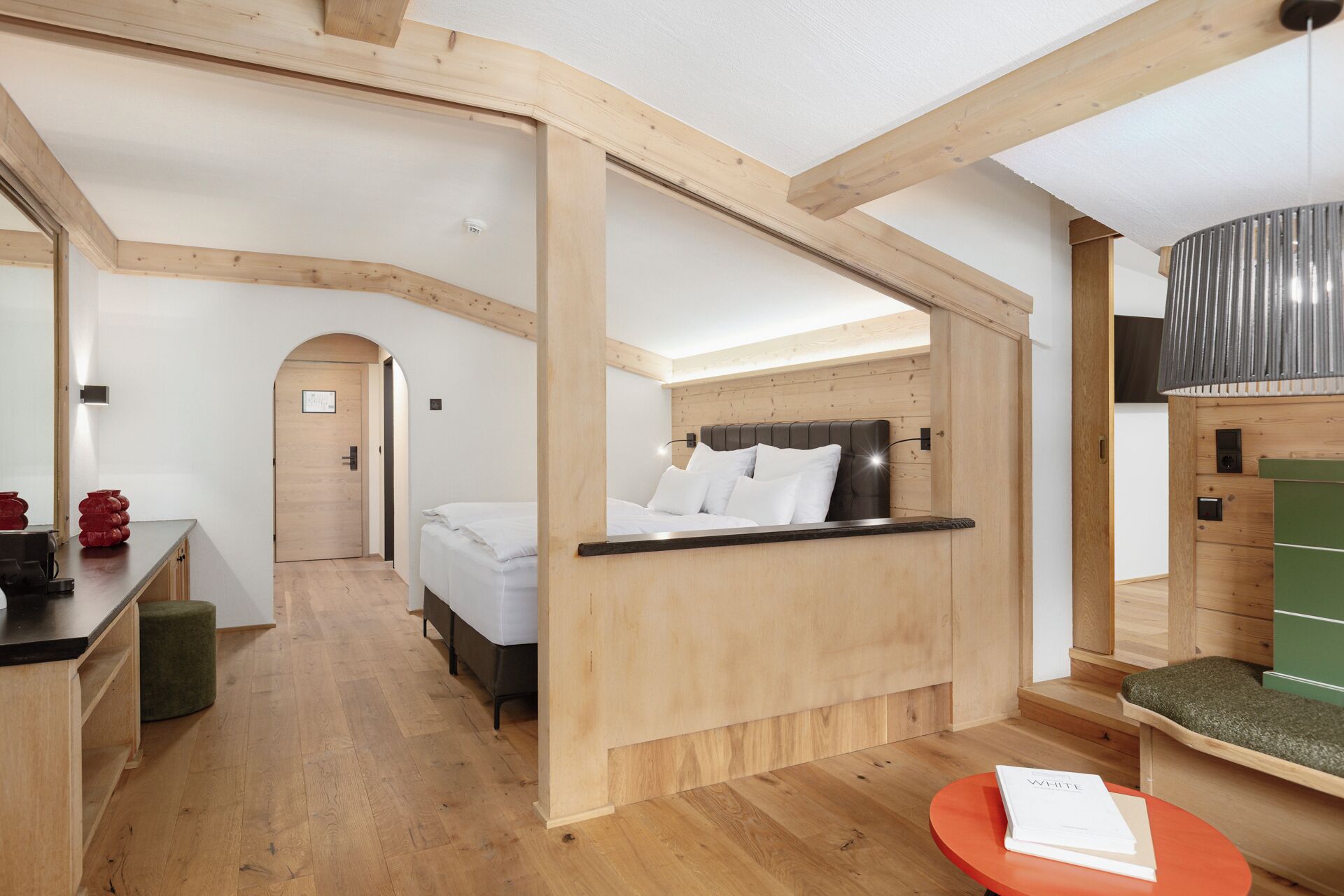 A modern hotel room with a wooden ceiling, a bed with white bedding, a small table with a book, and a green ottoman.