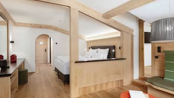 Ein modernes Hotelzimmer mit Holzbalkendecke, einem Bett mit weißer Bettwäsche, einem kleinen Tisch mit einem Buch und einem grünen Hocker.