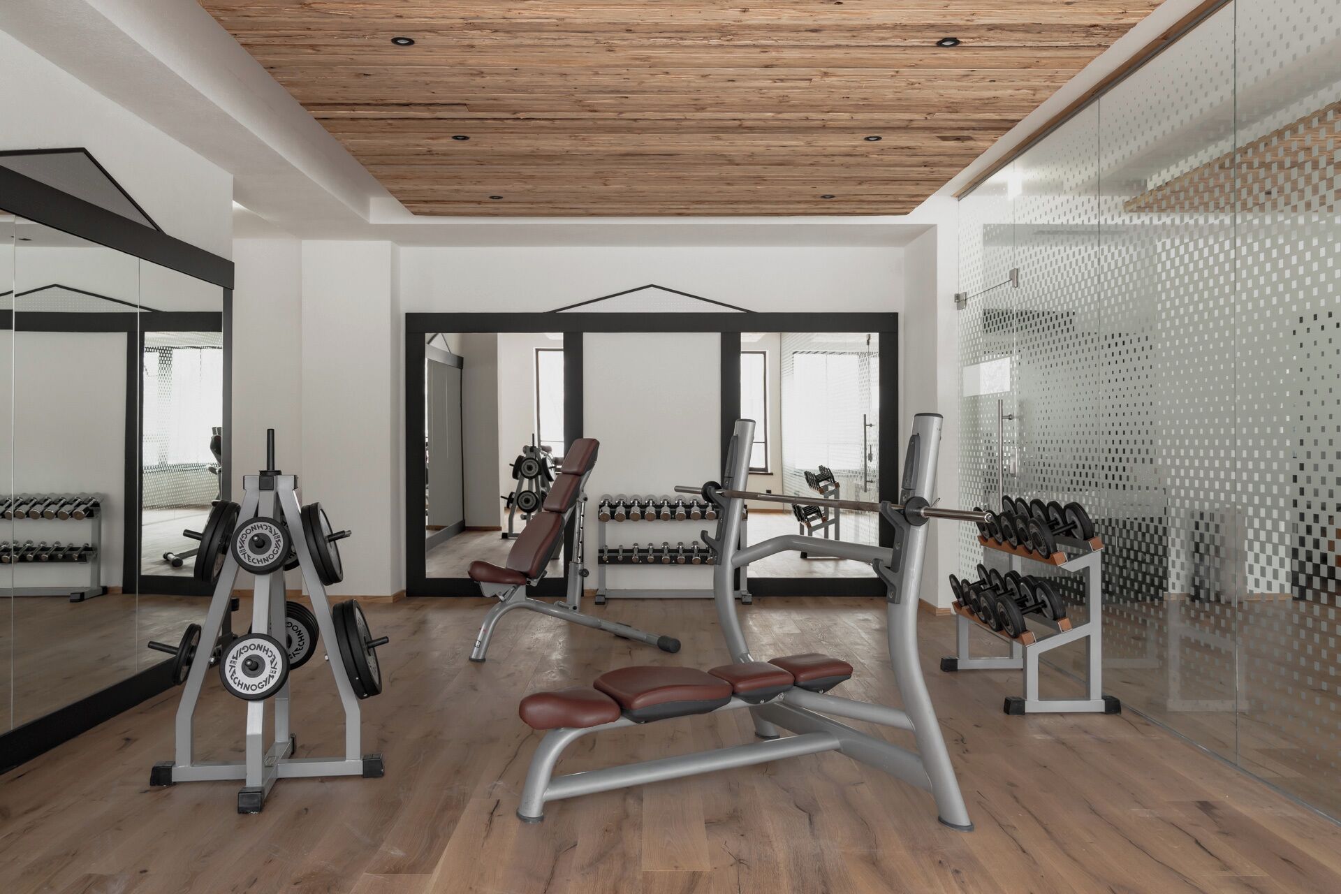 Uma academia com paredes espelhadas, piso de madeira e diversos equipamentos de exercício.