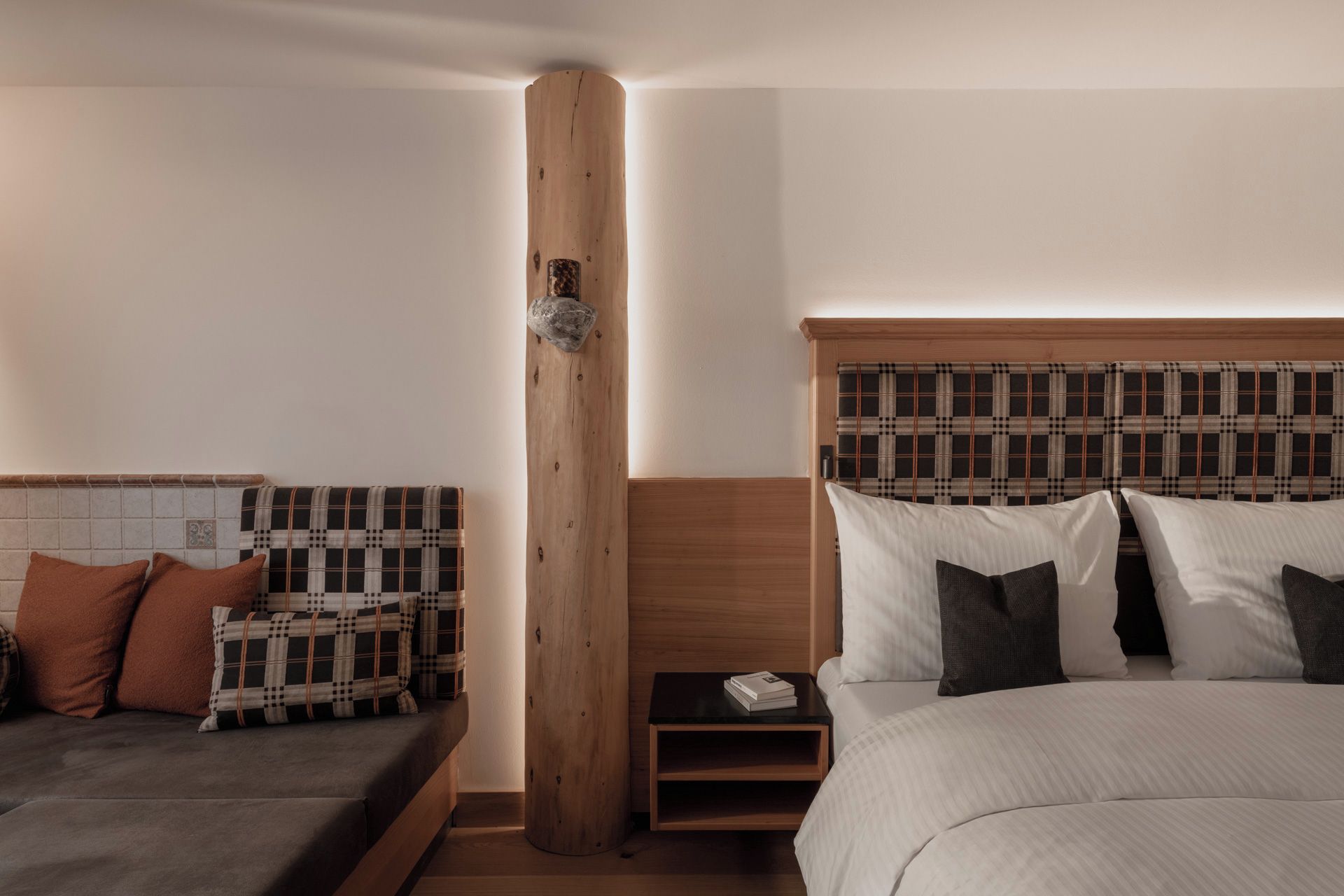 Ein Schlafzimmer mit einem Bett, einem Nachttisch, einer Holzsäule und einem Sofa.