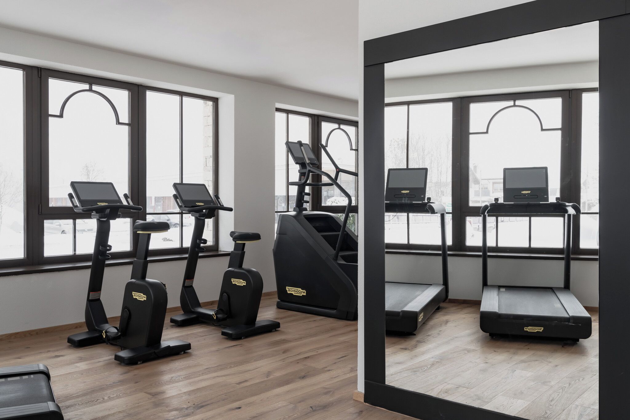 A gym with treadmills, elliptical machines, and a mirror reflecting the space.
