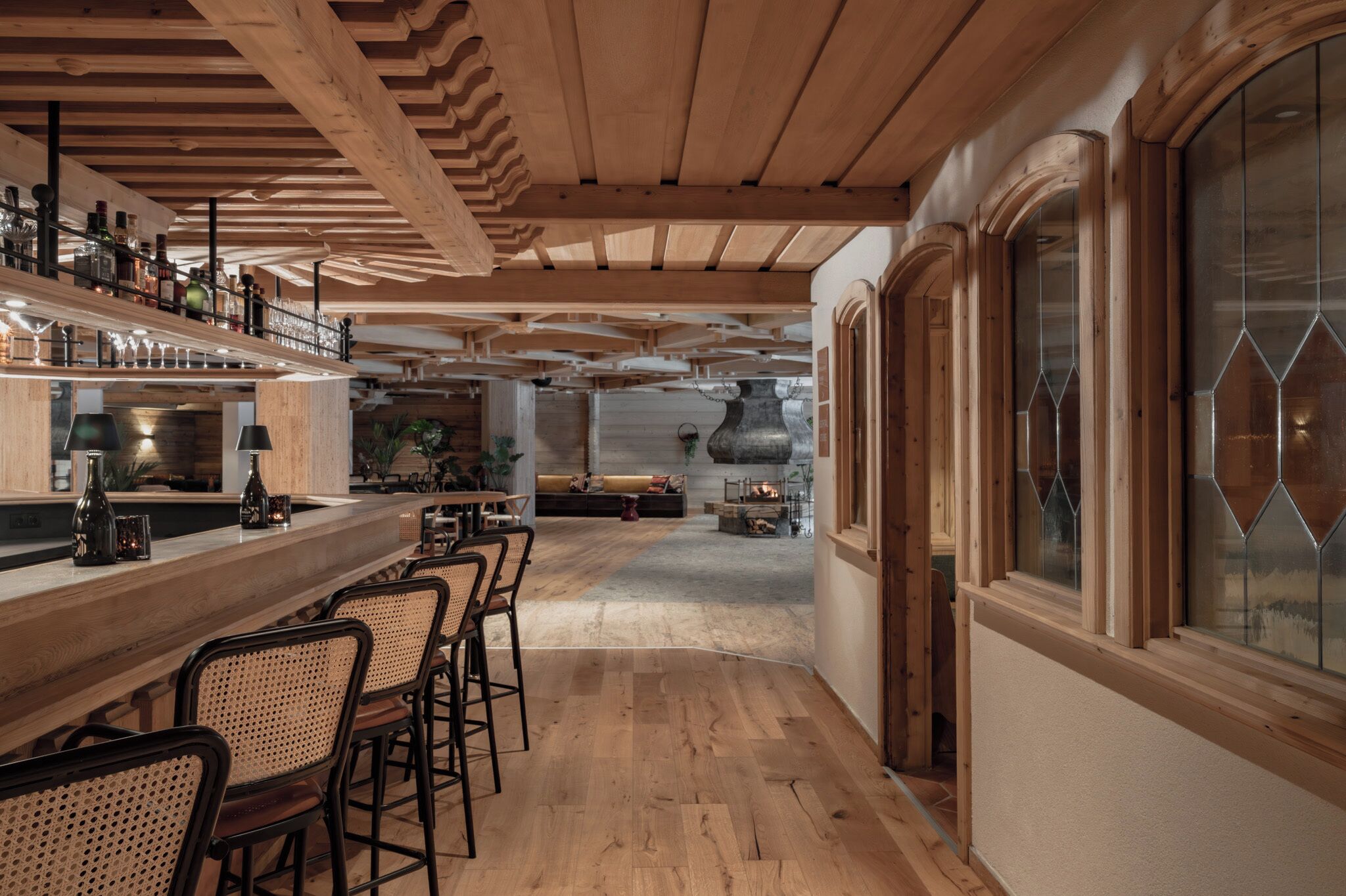 Un espace bar en bois, doté de sièges, d’une cheminée et de grandes fenêtres.