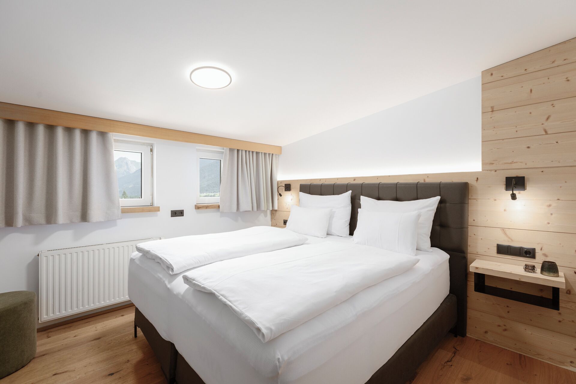Ein Hotelzimmer mit zwei Betten, einem hölzernen Kopfteil, einem Nachttisch, einem Spiegel und Blick auf die Berge.