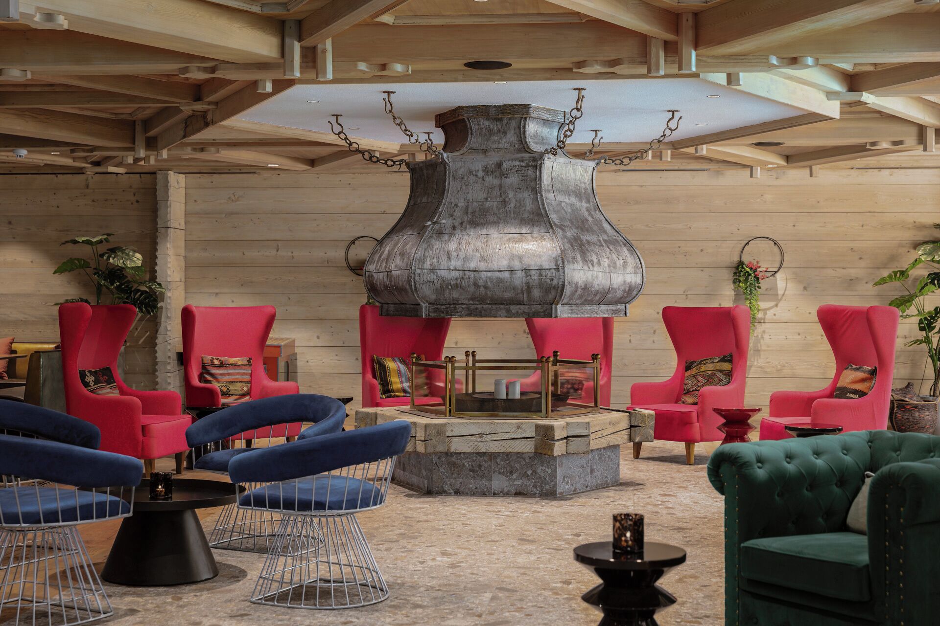 Un área de descanso con sillones rojo y azul, una chimenea de metal grande y un sofá verde.