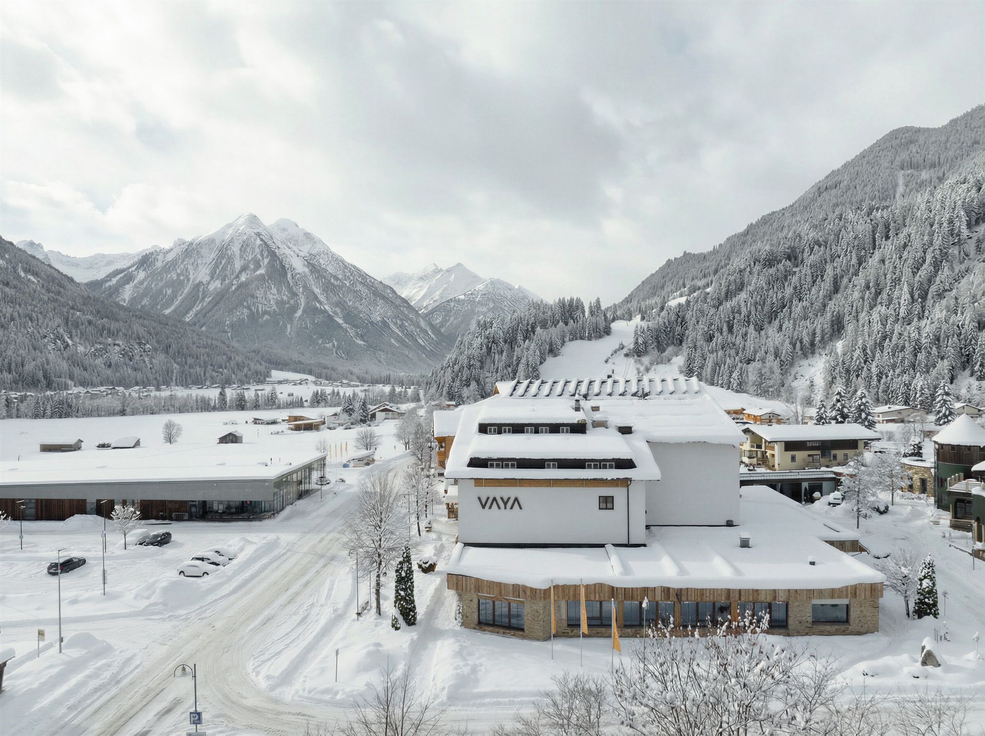 Ein schneebedecktes Bergresort mit einem markanten VAYA-Gebäude, umgeben von schneebedeckten Bäumen und Bergen.