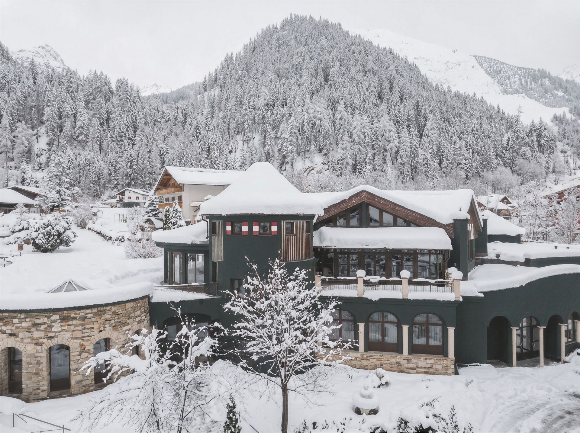 A large, multi-story building with a prominent balcony, surrounded by snow-covered trees and mountains.