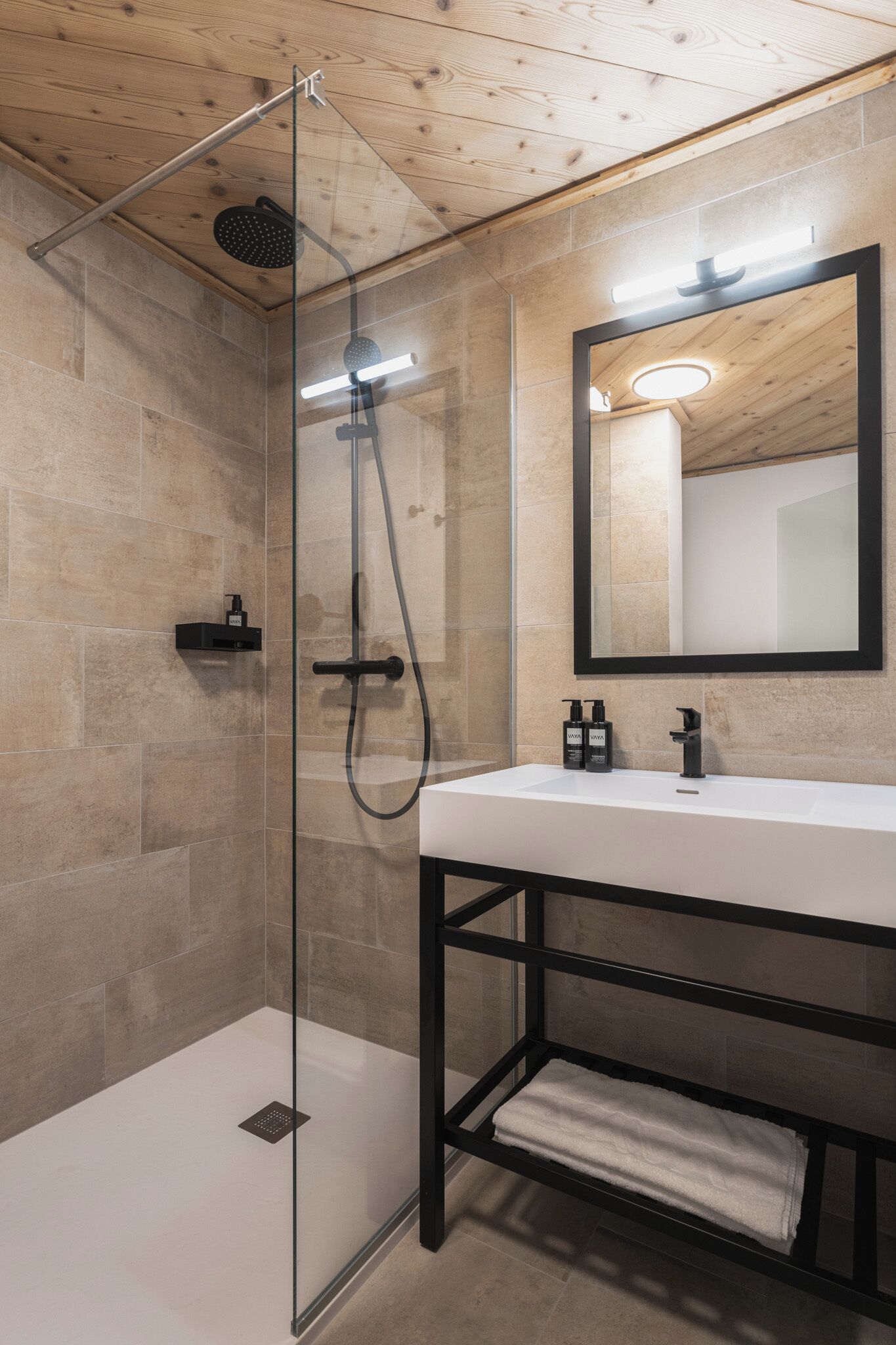Un baño moderno con cabina de ducha de vidrio, un espejo grande y un lavabo blanco.