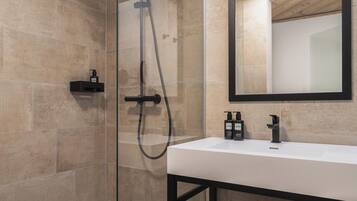 A modern bathroom with a glass-enclosed shower, a large mirror, and a white sink.