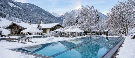A swimming pool surrounded by snow-covered trees and mountains in the background.