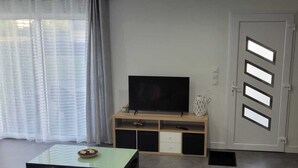 A living room with a flat-screen TV on a wooden stand, a glass coffee table, and a door with geometric cutouts.