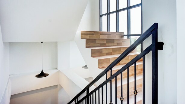 A modern staircase with wooden steps and black railings, leading to a landing with a hanging light fixture. - Capital O 94254 Dental Inn (Banda Aceh)