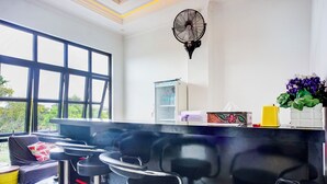 A kitchen with a black countertop, bar stools, a fan, a refrigerator, and a window with a view of greenery. - Capital O 94254 Dental Inn (Banda Aceh)