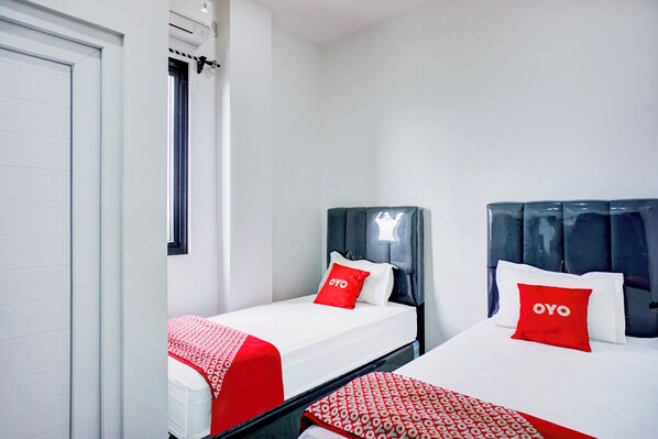 Two single beds with headboards, white bedding, red pillows with 'OYO' branding, and a window with curtains.