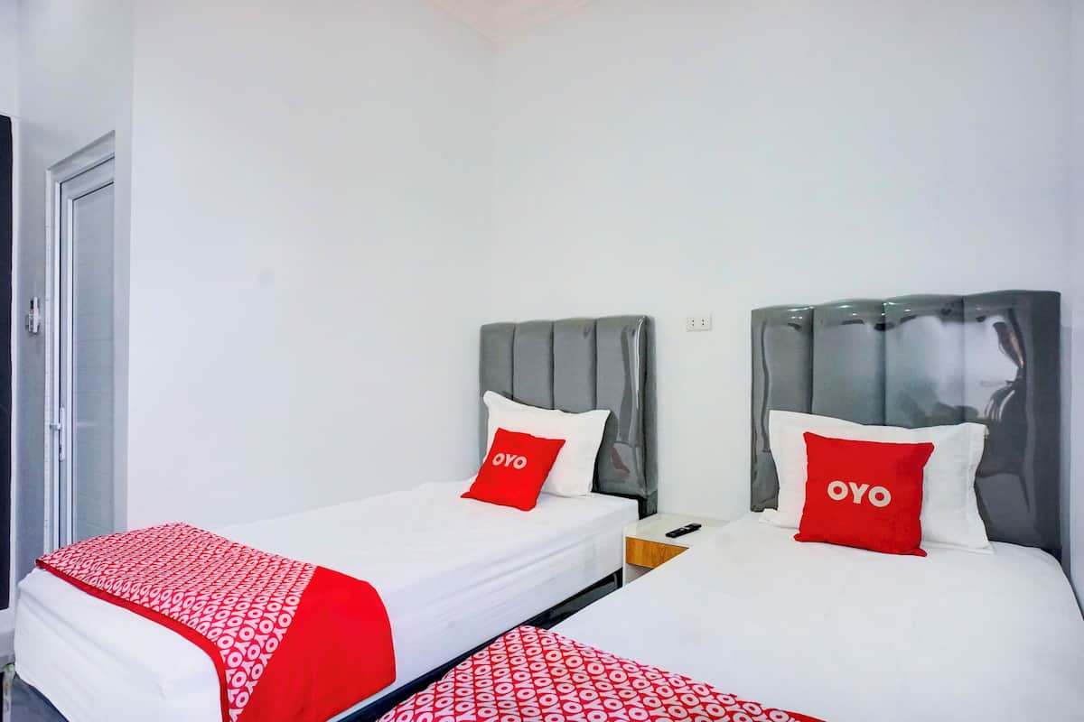 Habitación de hotel con dos camas, cada una con cabecero gris y ropa de cama blanca. Hay almohadas rojas con la palabra 'OYO' en ellas.