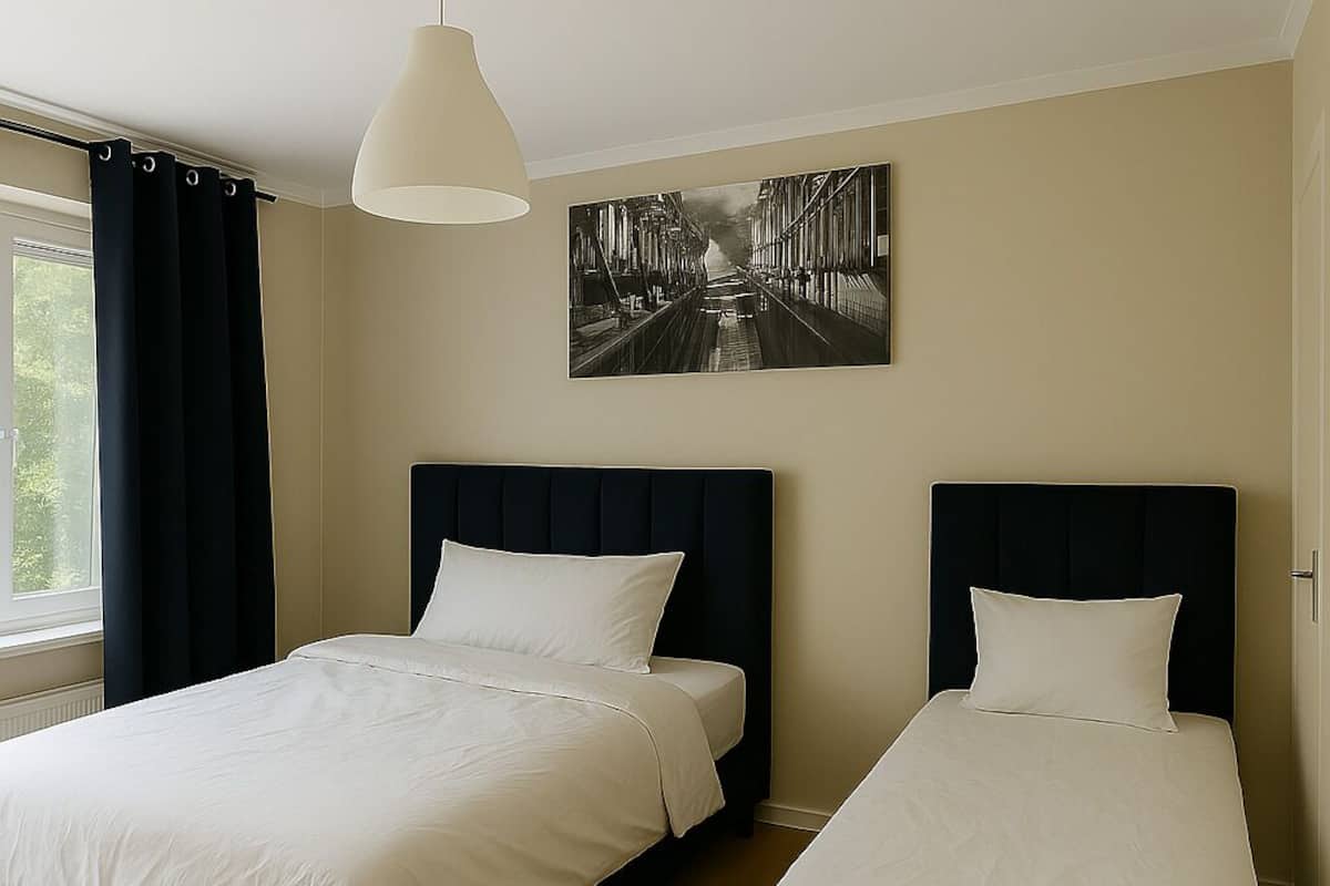 Una habitación de hotel con dos camas, un ventanal con cortinas, una lámpara colgante y un cuadro blanco y negro en la pared.