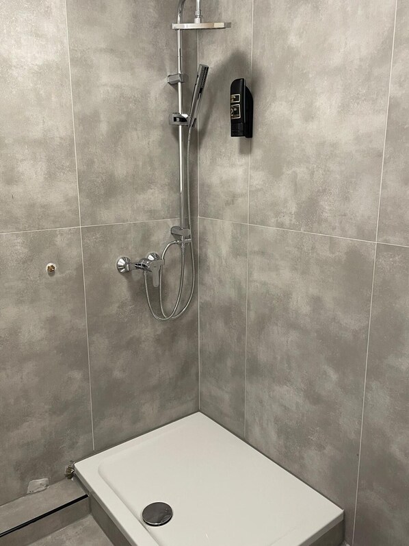 A modern shower with a handheld showerhead, a wall-mounted control panel, and a white bathtub. - Haven Hotel Wuppertal (Wuppertal)