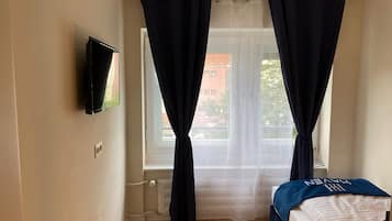 A bedroom with a bed, a TV mounted on the wall, and a window with curtains.