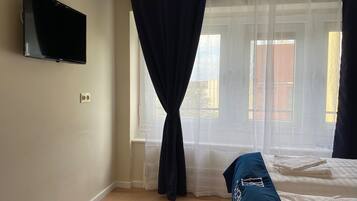 Un dormitorio con una cama, un televisor montado en la pared y un ventanal con cortinas de gasa.