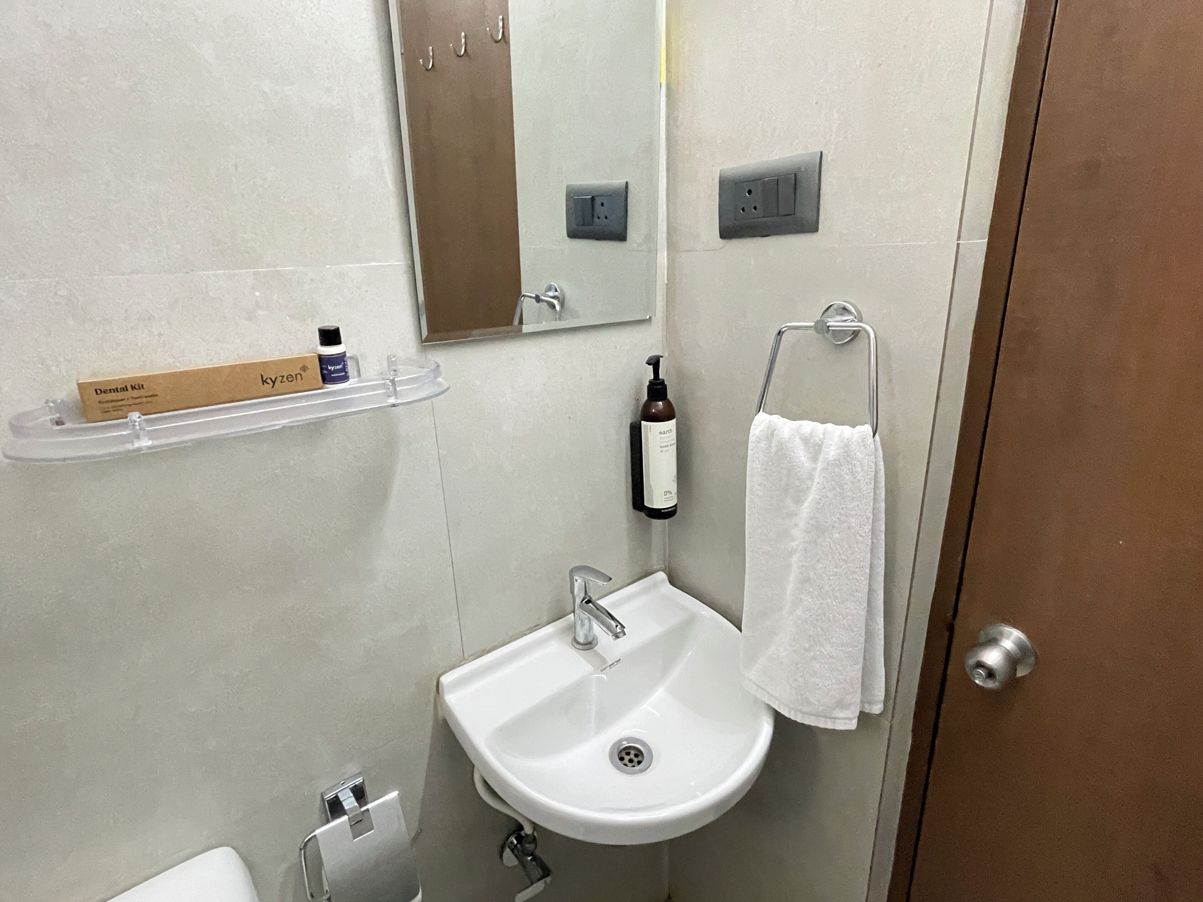 A bathroom with a white sink, a mirror, a towel rack, a shelf with toiletries, and a door.