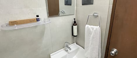 A bathroom with a white sink, a mirror, a towel rack, a shelf with toiletries, and a door.