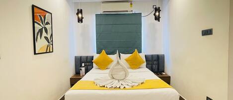 A modern hotel room with a large bed, bedside tables, a wall-mounted air conditioner, and a ceiling light fixture.