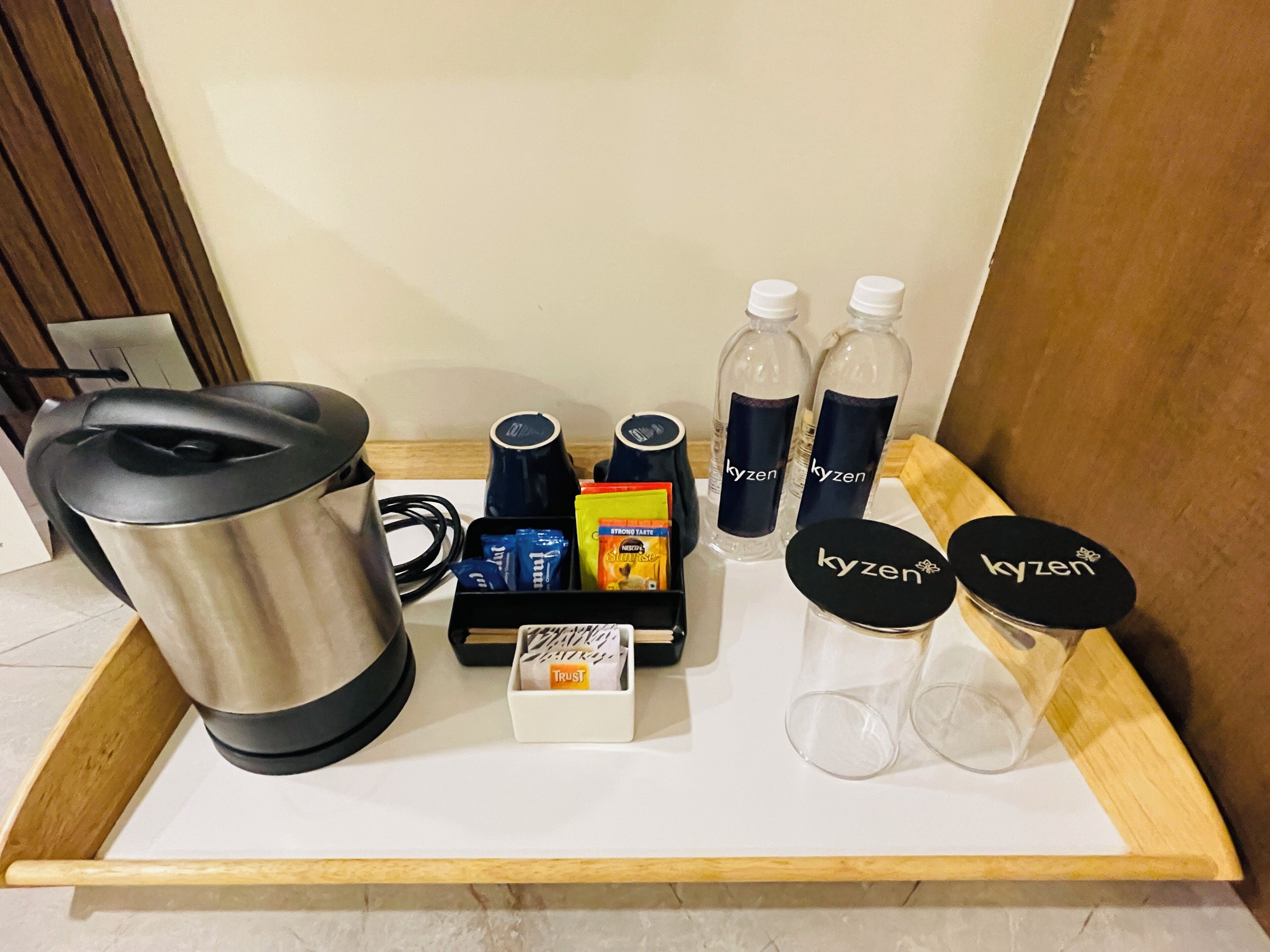 Een dienblad met een waterkoker, koffiezetapparaat, waterflesjes, snacks en glazen met de aanduiding 'kyzen'.