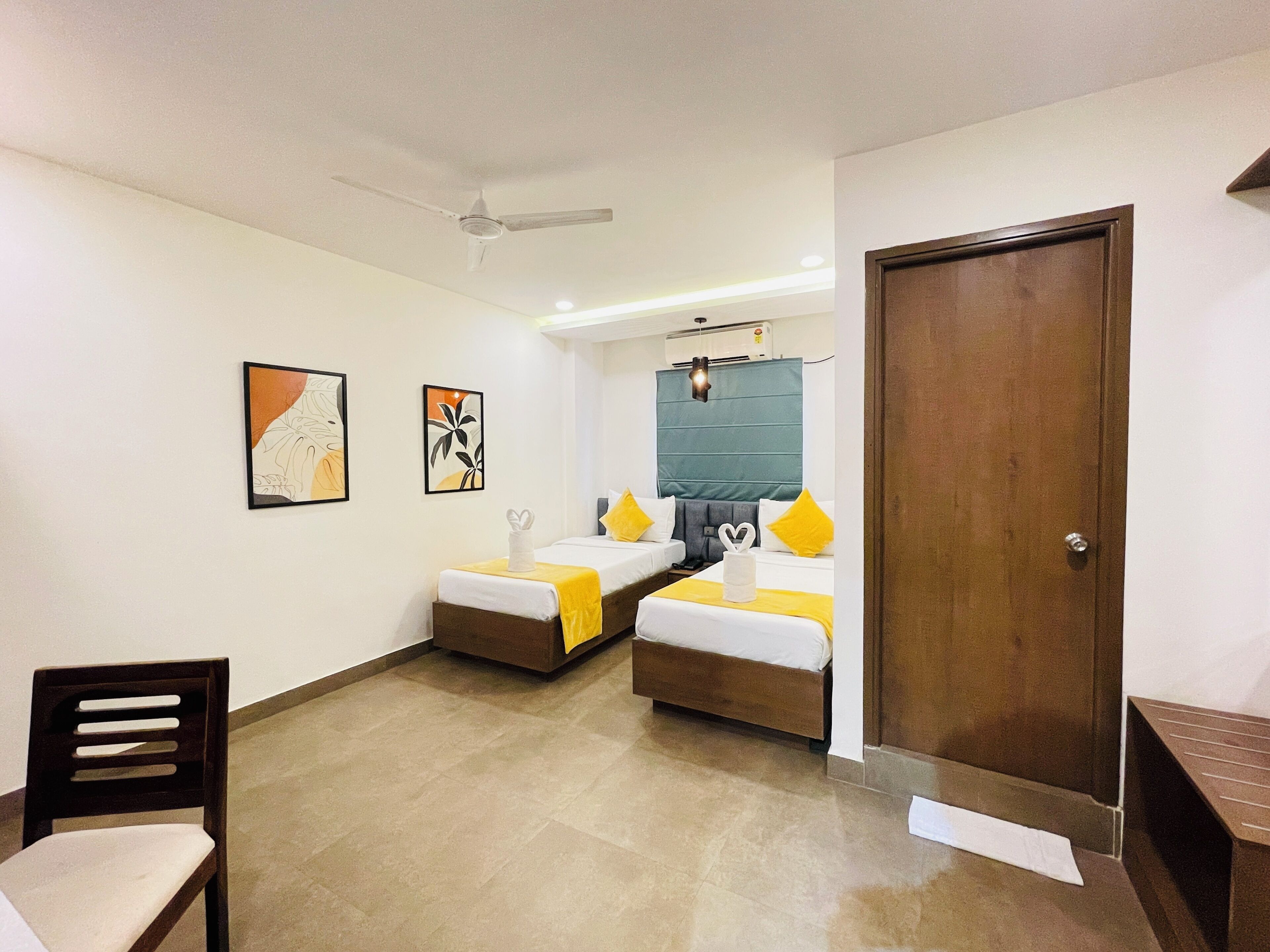 A hotel room with two beds, a ceiling fan, artwork on the walls, and a wooden door.