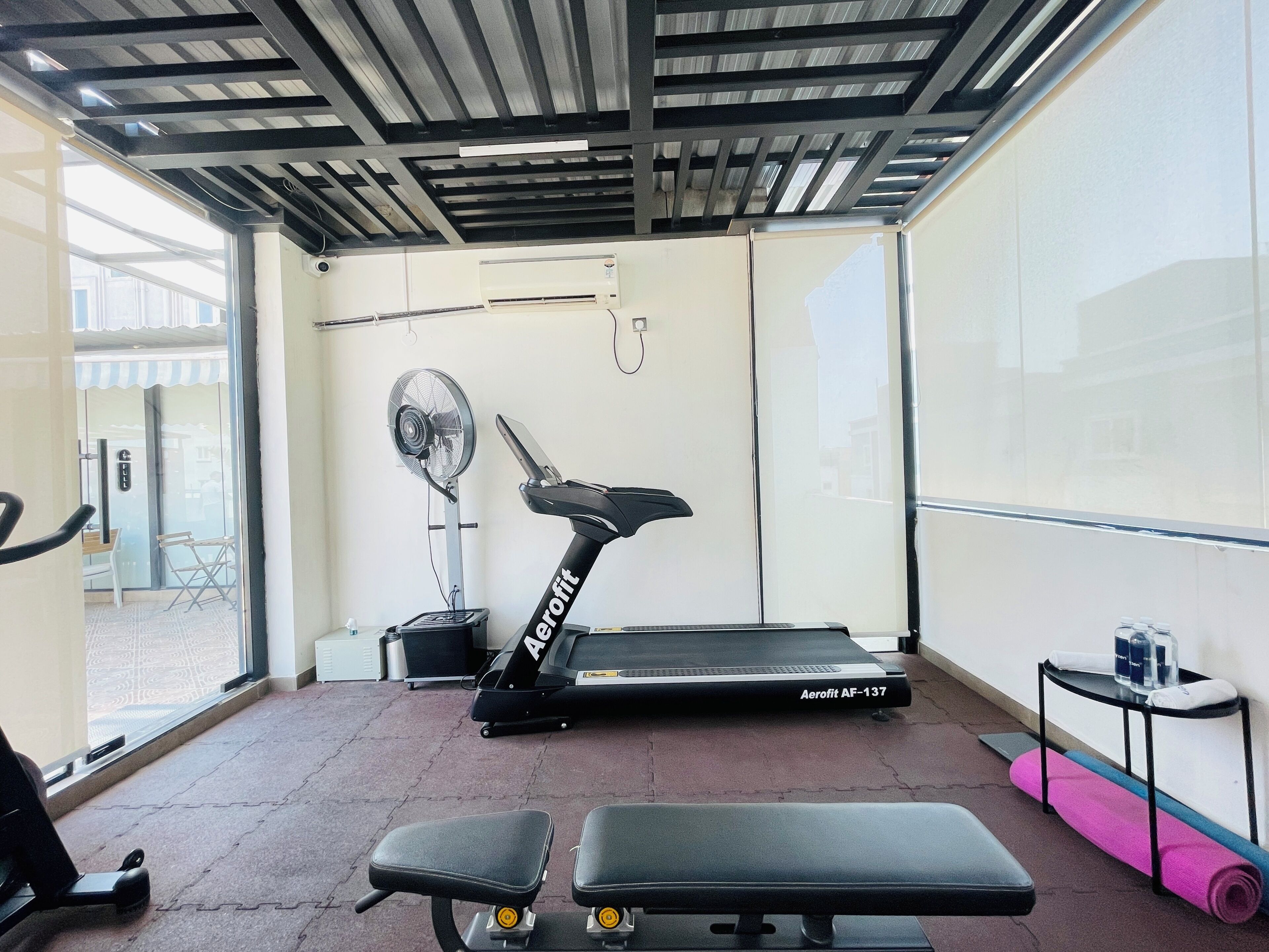 A gym with a treadmill, benches, a fan, and a window with a view.