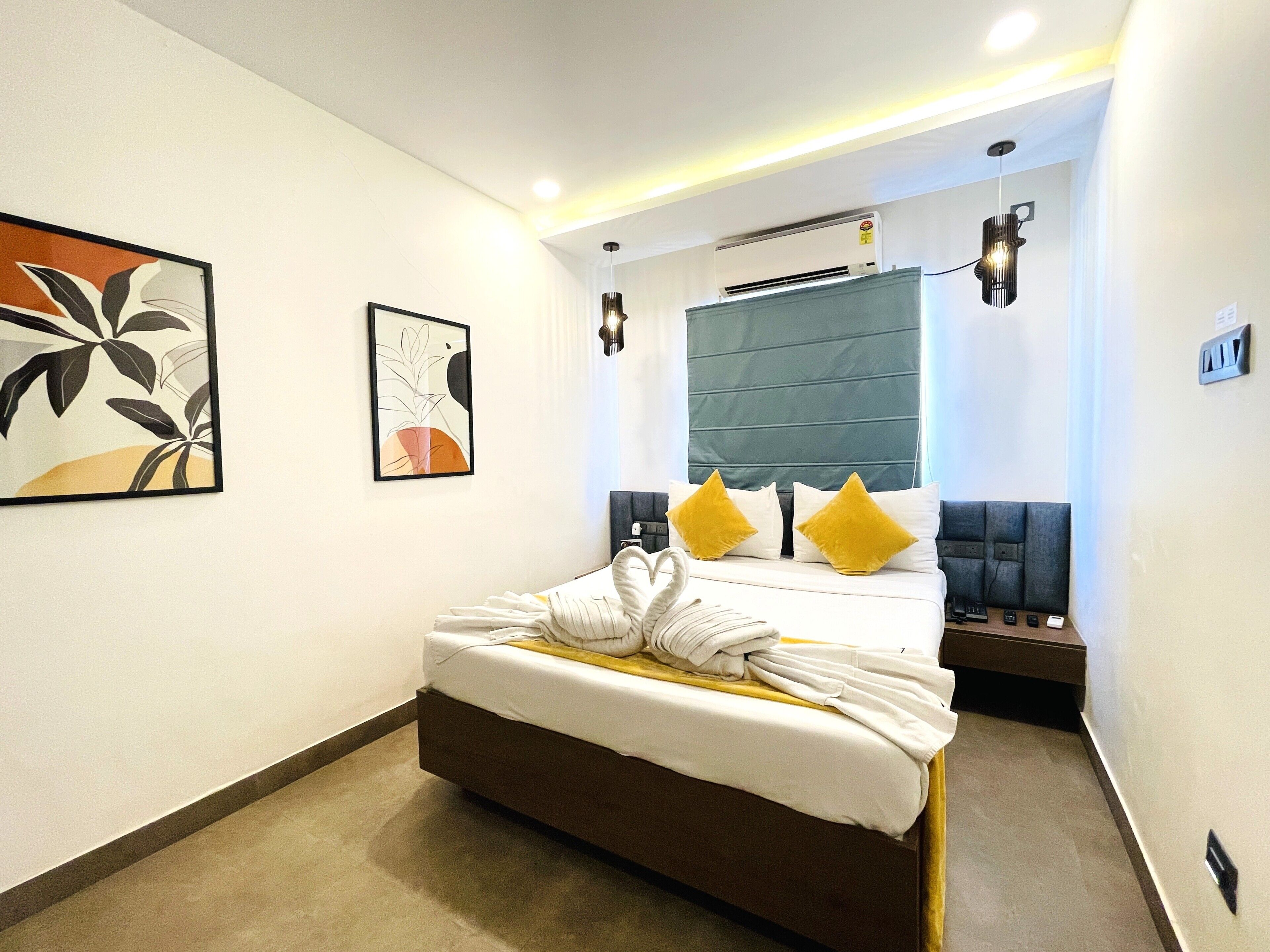 A hotel room with a bed, a headboard, a wall-mounted air conditioner, and a framed abstract painting.