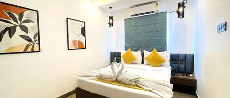A hotel room with a bed, a headboard, a wall-mounted air conditioner, and a framed abstract painting.