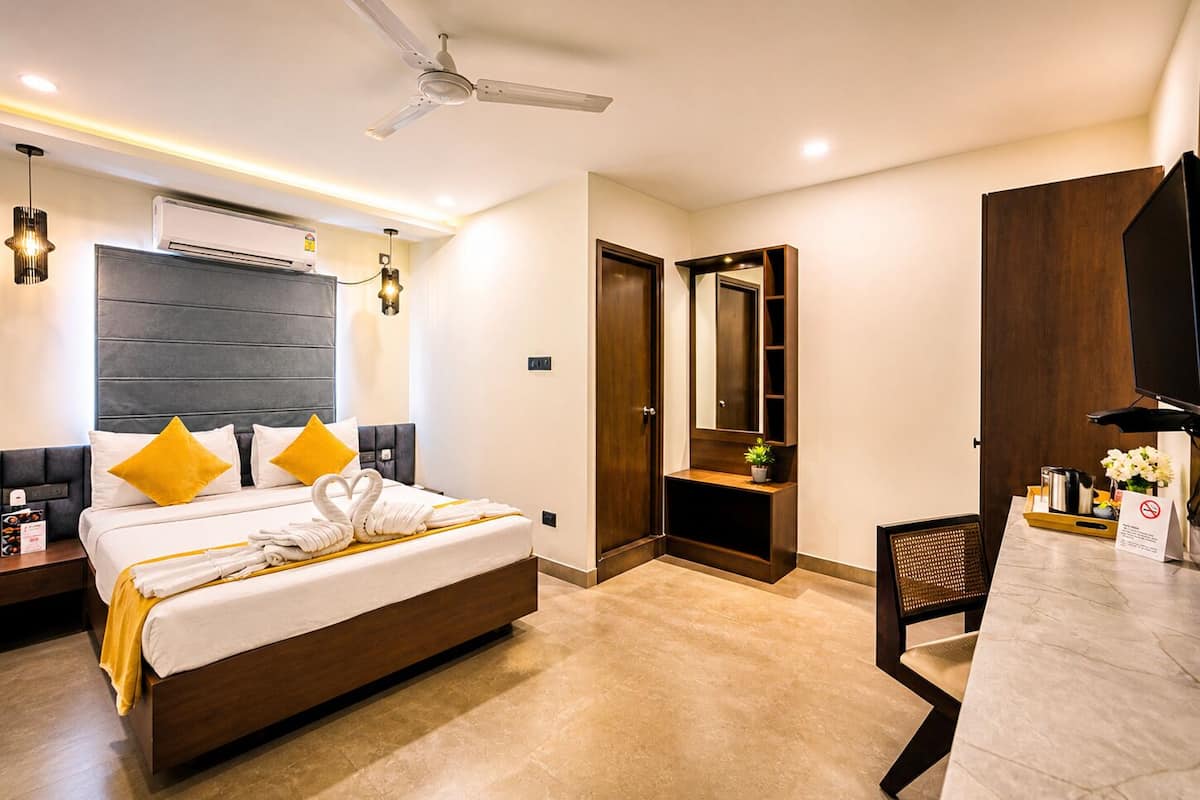 Ein Hotelzimmer mit Bett, Schreibtisch, Stuhl, Deckenventilator, Klimaanlage und Spiegel.