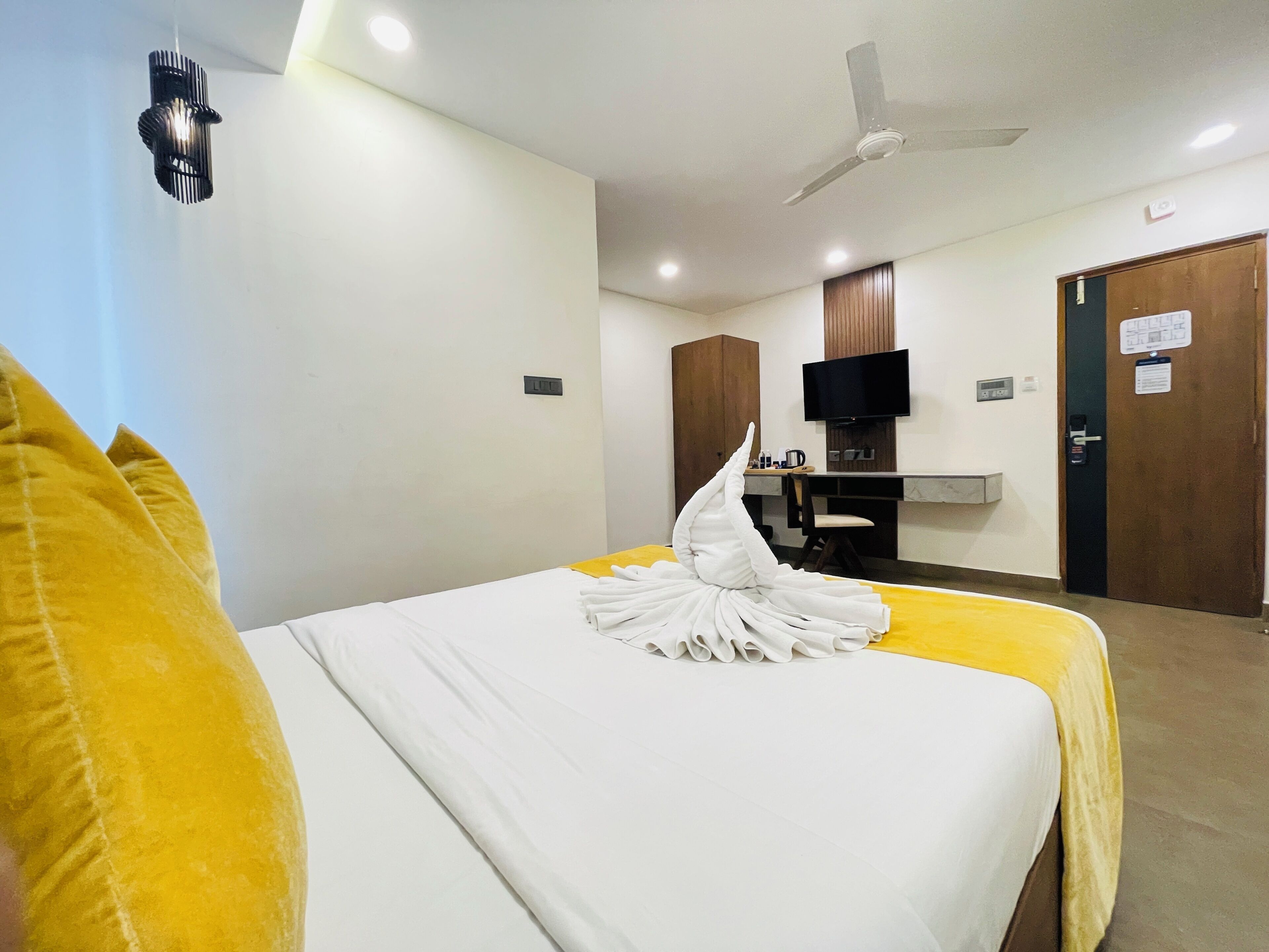 Una habitación de hotel con cama, escritorio, televisor y ventilador de techo.