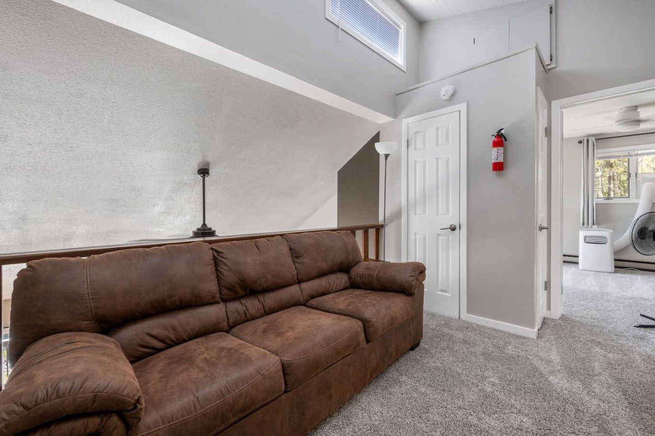 A room with a brown leather sofa, a white door, a white radiator, and a white ceiling vent.