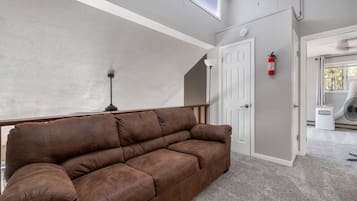 A room with a brown leather sofa, a white door, a white radiator, and a white ceiling vent.